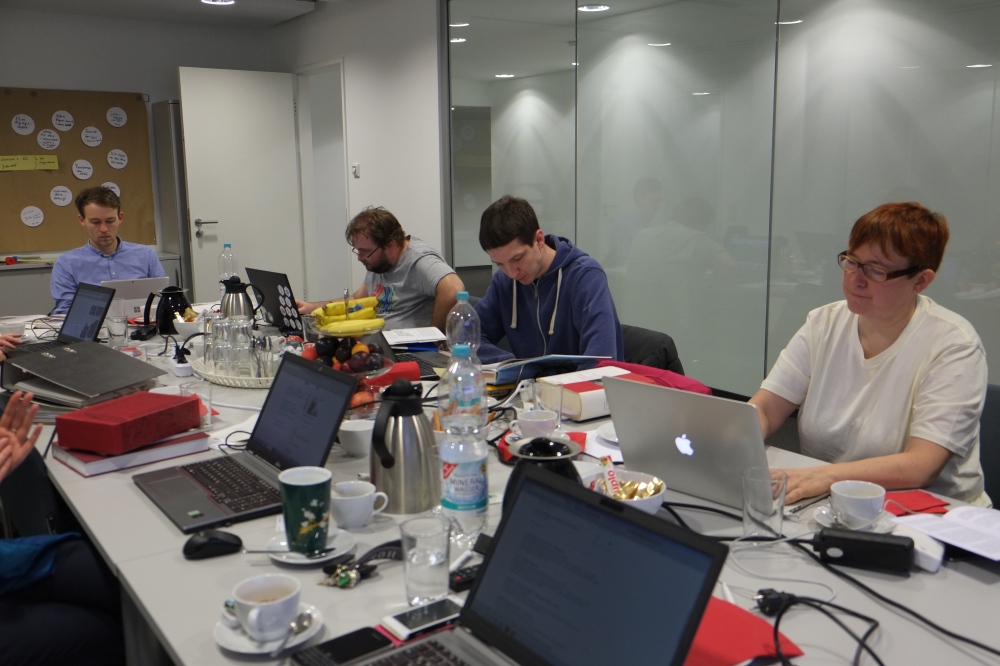 4 Personen arbeiten konzentriert an ihren Notebooks. Die Tischfläche wird voll genutzt - mit Technik und Kaffee.