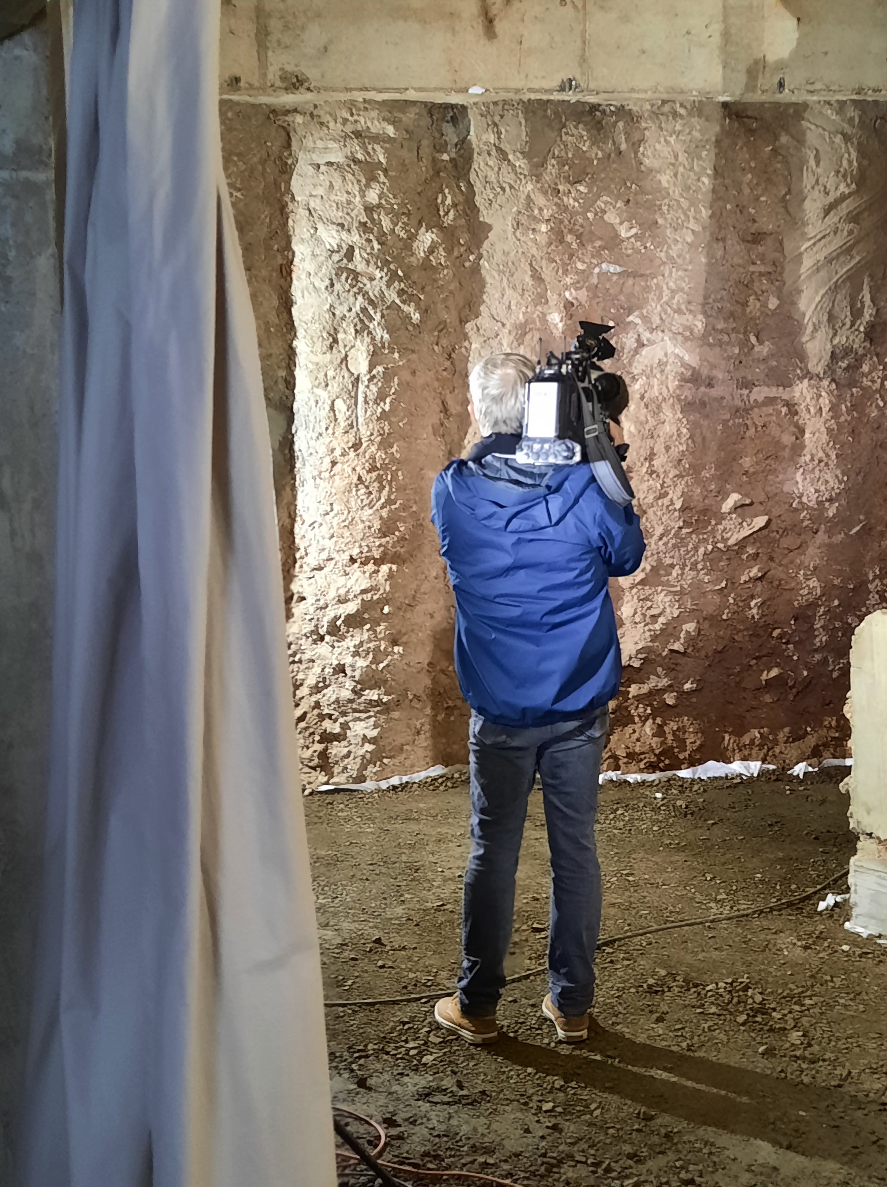 Ein Mann in blauer Jacke macht Filmaufnahmen von der Bohrpfahlwand, die die Baustelle im Untergrund umgibt.