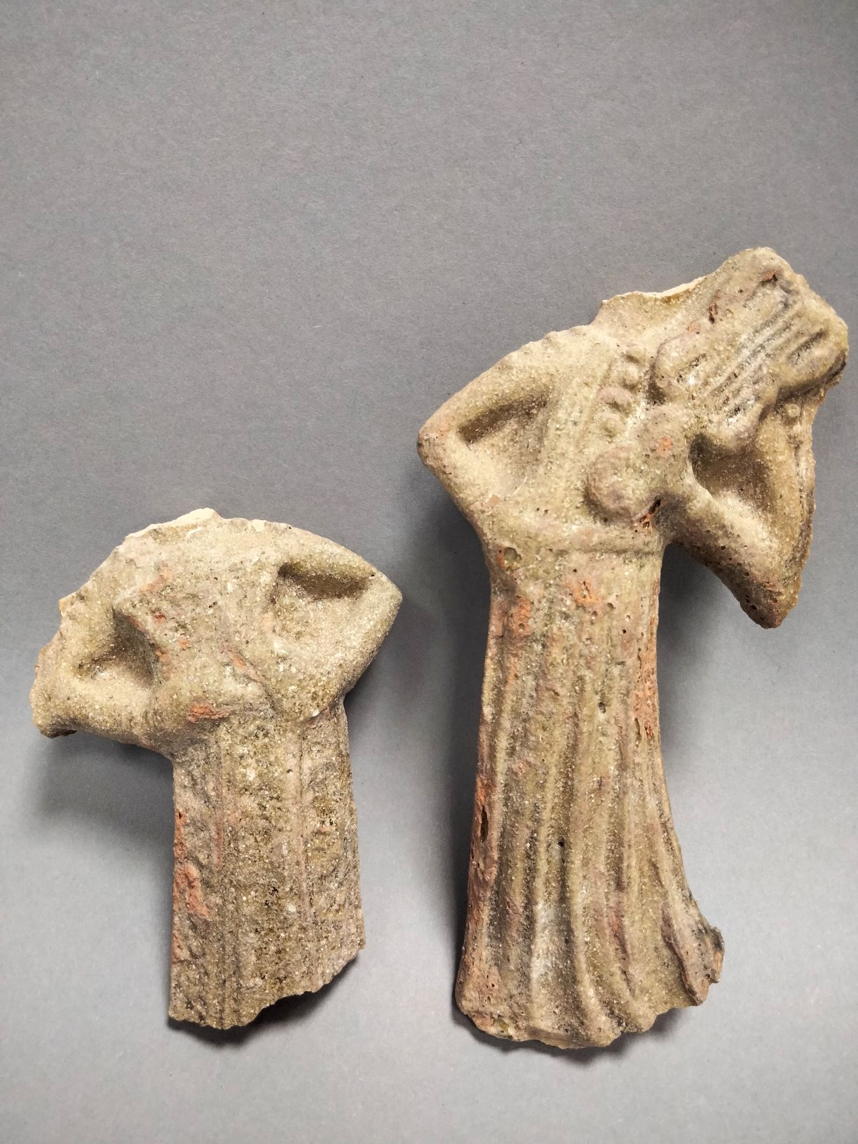 Foto von einer archäologischen Fundgruppe bestehend aus zwei figürlichen Darstellungen. Beiden steinernen Figuren fehlt der Kopf. Leichte Farbreste sind erkennbar.